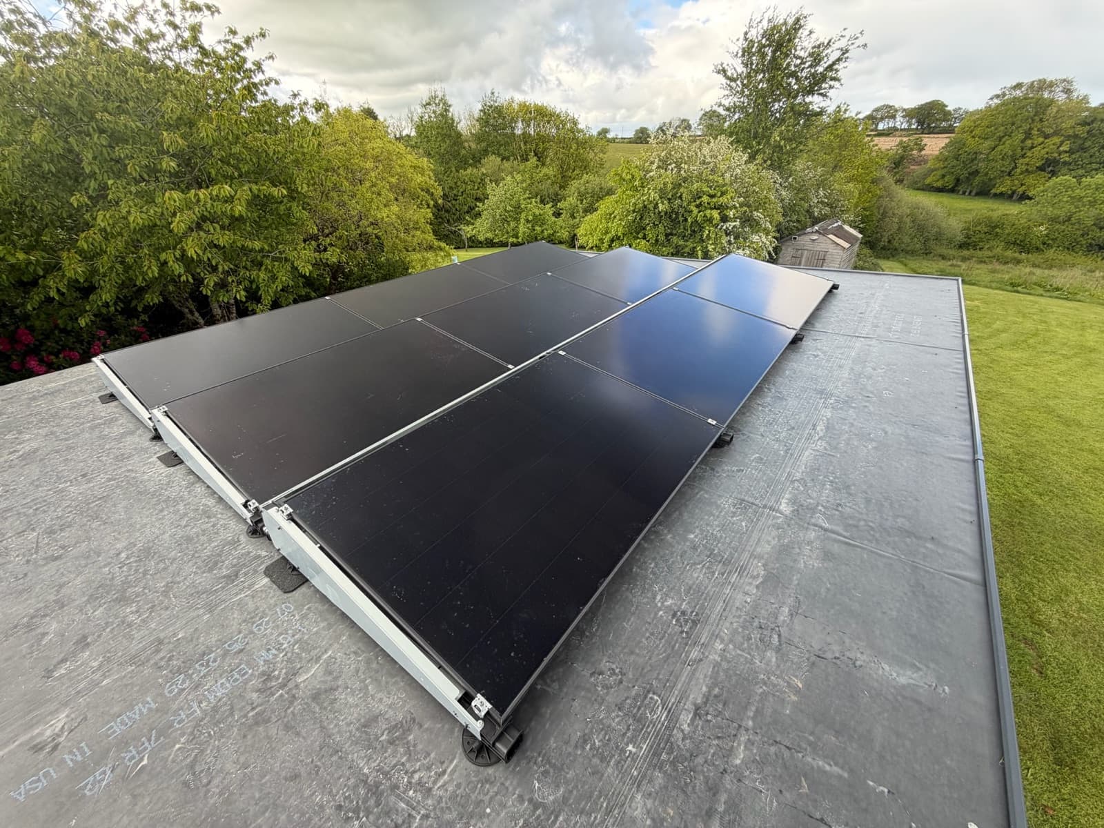 Panels on ballasted frames across a flat roof, with open countryside behind.